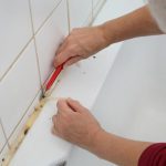 Removing silicone caulk from bathroom tiles with a razor.